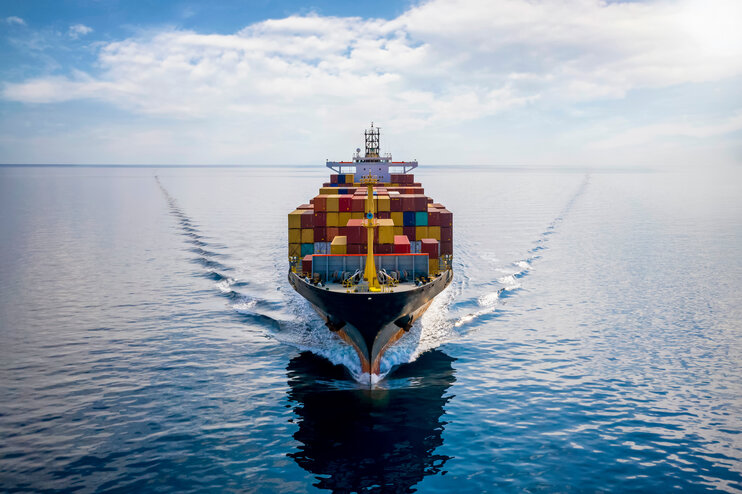 Luftaufnahme von vorne: Beladenes Containerschiff fährt über ruhigen Ozean