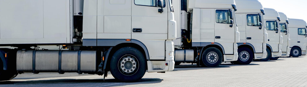 Buchhaltung / Finance Operations (m/w/d) Mehrere weiße LKWs einer Spedition stehen geparkt nebeneinander auf dem Betriebshof.