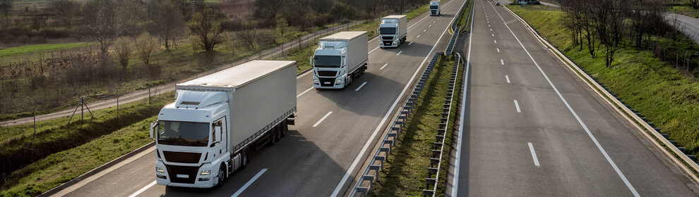 Konvoi von Lastwagen auf einer Landstraße in ländlicher Umgebung.