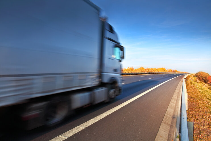 Weißer LKW fährt durch herbstliche Landschaft mit buntem Laub.